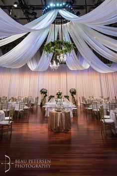 the ceiling is decorated with white draping and greenery for an elegant wedding reception