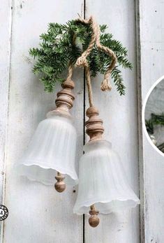 two white bells hanging from the side of a wooden door with pine cones and twine