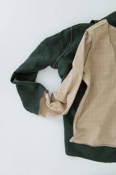 a green and brown jacket laying on top of a white surface