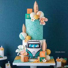 a vw bus cake with flowers on top sits on a table next to cupcakes