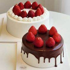 two cakes with chocolate frosting and strawberries on the top one is covered in white icing