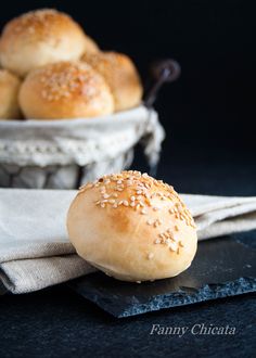 bread rolls with sesame seeds sit in a basket next to a napkin on a table