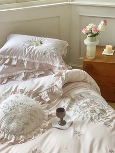 a bed with white sheets and pink flowers in a vase on the end table next to it