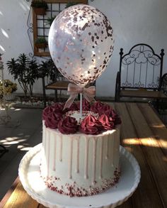 a large white cake with red flowers and a giant balloon on top is sitting on a wooden table