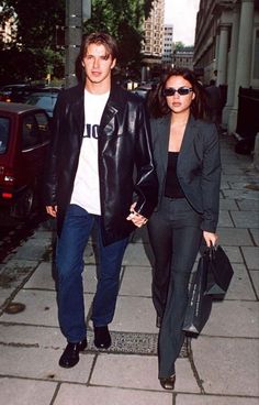 a man and woman are walking down the sidewalk together, one is carrying a handbag