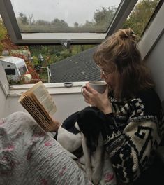 a woman sitting on a window sill reading a book and holding a coffee cup