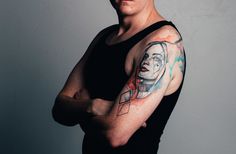 a man with a tattoo on his arm and shoulder standing in front of a gray wall