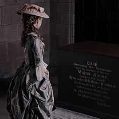 a woman in a long dress and hat standing next to a plaque with writing on it