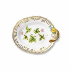 a white plate with green leaves and flowers on the rim, holding a golden handle