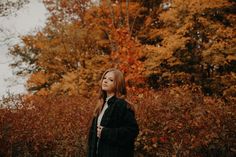 a woman standing in front of trees with orange leaves on it's fall foliage