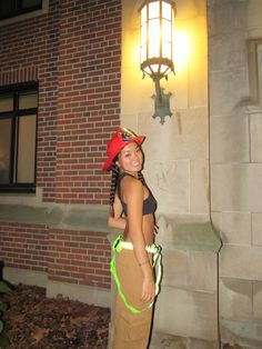 a woman standing in front of a brick building wearing a red hat and brown pants