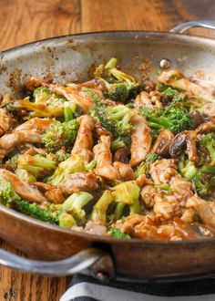 chicken and broccoli stir fry in a wok on a wooden table top