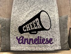 a grey pillow with the word cheer on it and a black megaphone in purple