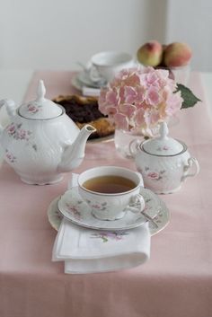 a table topped with plates and cups filled with tea next to a vase full of flowers