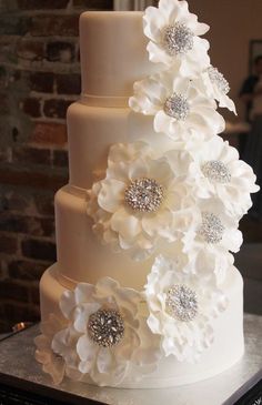 a three tiered wedding cake with white flowers on the top and silver crystals in the middle