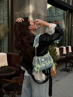 a woman standing on the sidewalk taking a photo with her cell phone while wearing a purse