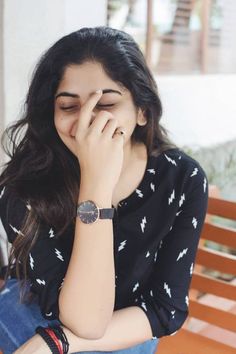 a woman sitting on a wooden bench holding her hand to her face with both hands