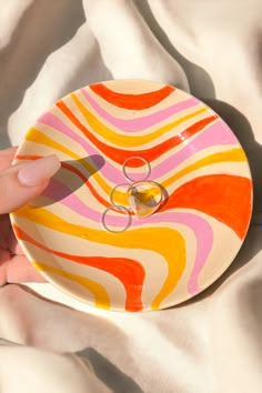 two wedding rings are placed on top of an orange and pink swirl patterned ring dish