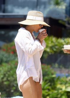 a woman in a white shirt and hat drinking from a cup