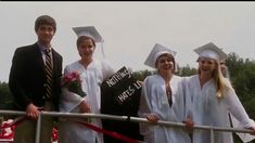 four people in graduation gowns and caps standing on a railing with ribbon around them