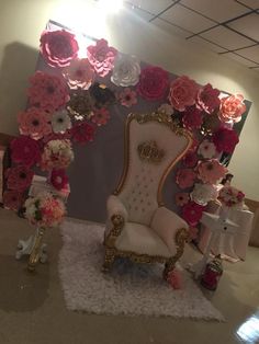 a fancy chair sitting in front of a wall with paper flowers on it and a mirror behind it