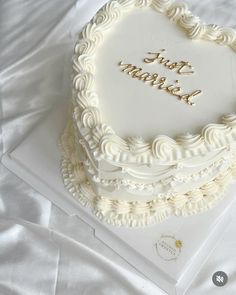 a heart shaped cake with the words just married on it sitting on a white sheet