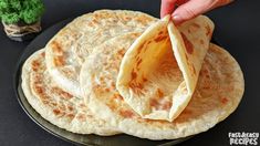 there is a hand that is holding a tortilla on a black plate with a potted plant in the background