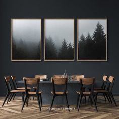 a dining room table and chairs with three paintings on the wall above it that have trees in the fog