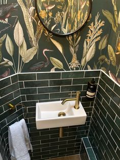 a sink and mirror in a small room with green tiles on the walls, along with wallpaper