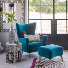 a blue chair and foot stool in front of a large window with an ornate mirror