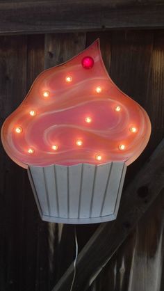 a cupcake shaped light hanging from the side of a wooden fence with lights on it