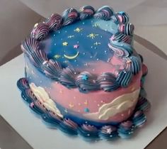 a blue and pink cake sitting on top of a white plate with stars and clouds