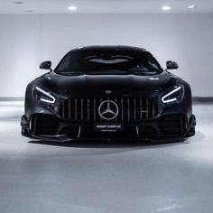 the front end of a black mercedes sports car in a white room with lights on