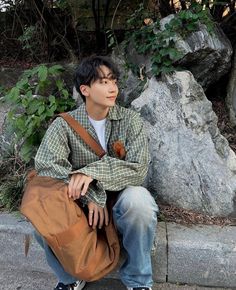 a young man is sitting on the curb with his handbag in front of him