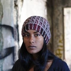 a woman wearing a knitted hat standing in front of a graffiti covered wall and looking at the camera