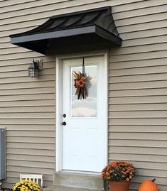 a white door with a black awning and some pumpkins on the front steps