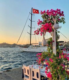 a table set up with flowers and plates next to the water in front of a boat