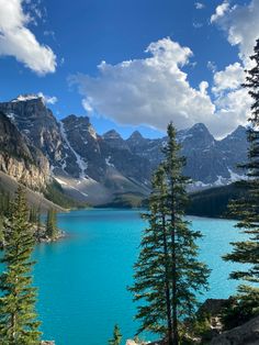 a lake surrounded by trees and mountains under a blue sky with white clouds in the background