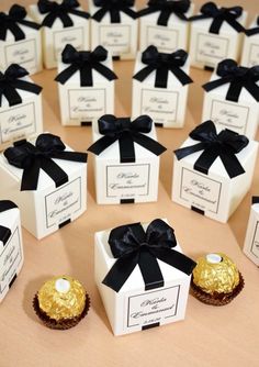 small white boxes with black bows and chocolates in them are sitting on a table