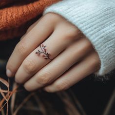 a woman's hand with a small flower tattoo on her left ring, and an orange sweater in the background