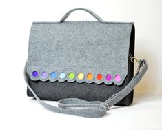 a gray felt bag with multicolored buttons on the front and shoulder strap, sitting on a white surface