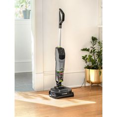 a black and silver vacuum sitting on top of a wooden floor next to a potted plant