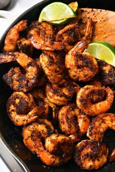 a skillet filled with shrimp and limes next to a wooden spoon on top of a table