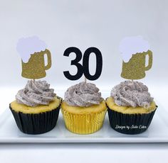 three cupcakes with frosting are on a white plate and the number 30 is placed next to them