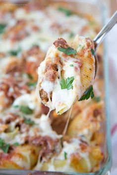 a spoon full of pasta with meat and cheese on it, being lifted from a casserole dish