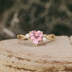 a pink heart shaped diamond ring on top of a rock