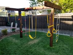 an outdoor play area with swings and climbing ropes in the grass next to a fence