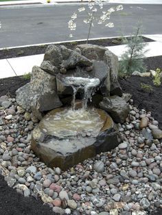 a small waterfall in the middle of a rock garden with gravel and rocks around it