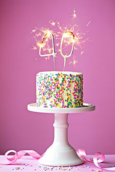 a birthday cake with sprinkles and sparklers on top, sitting on a pedestal