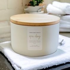 a white jar sitting on top of a counter next to towels and a potted plant